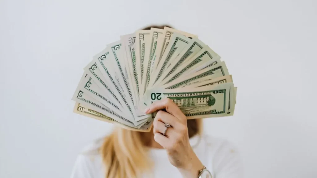 A woman showing dollars in front of her face to describe how to make $10K per month as a passive income