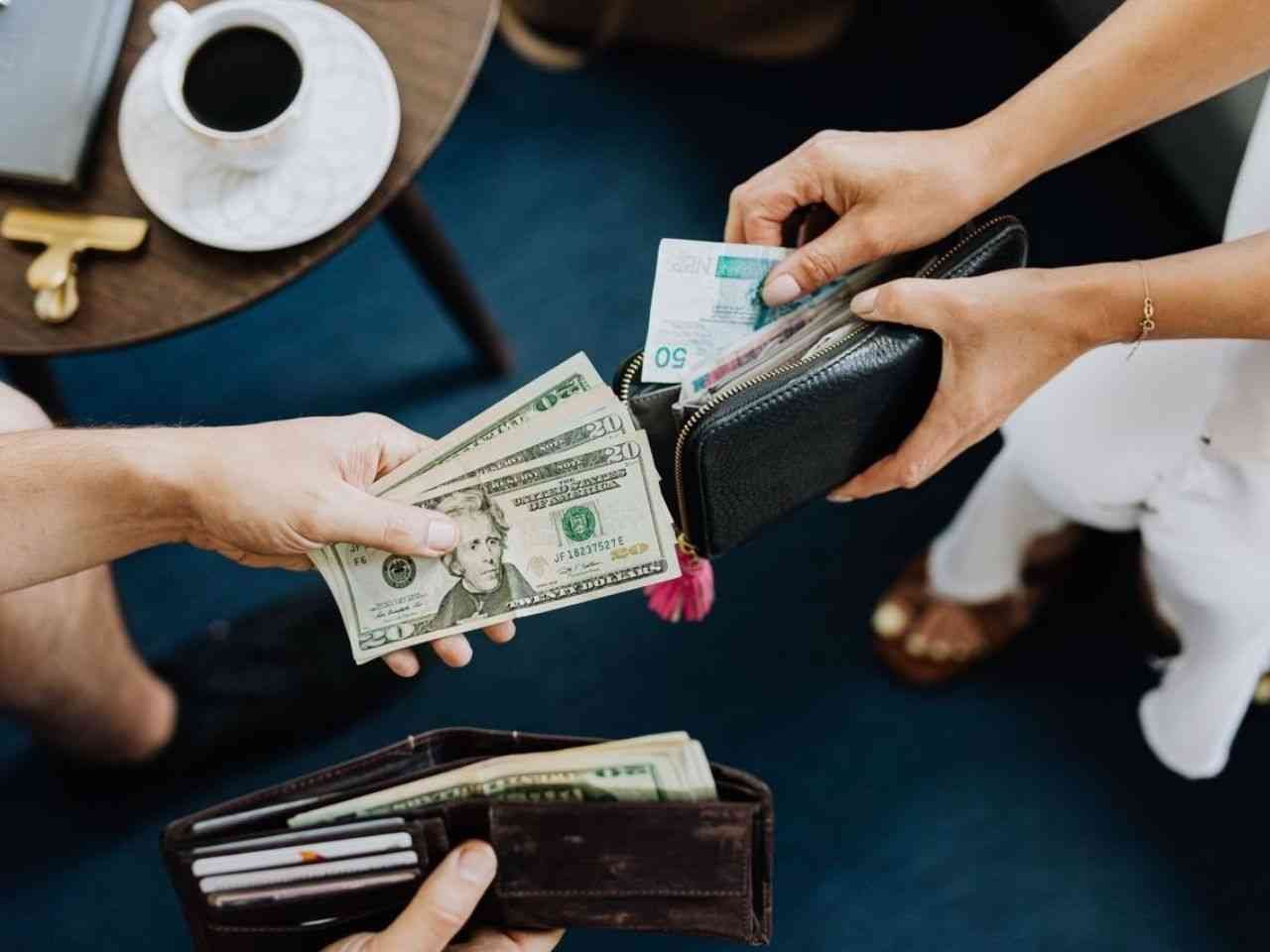 Close-up of two people exchanging US dollars and currency with wallets on a table